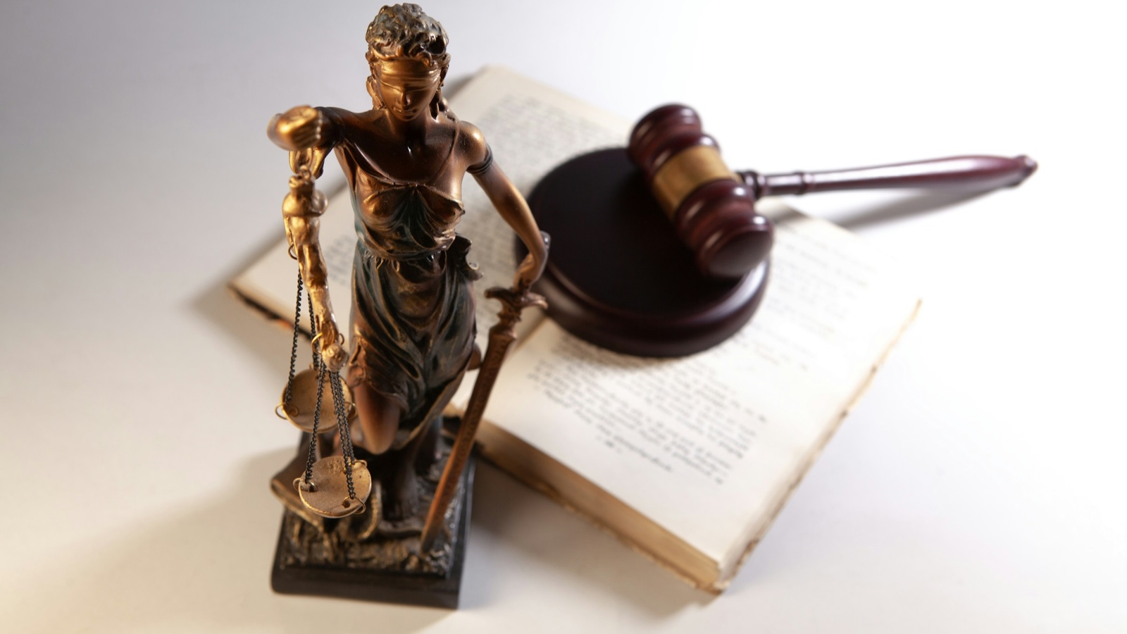 A bronze statue of Lady Justice standing in front of a wooden gavel on an open law book.