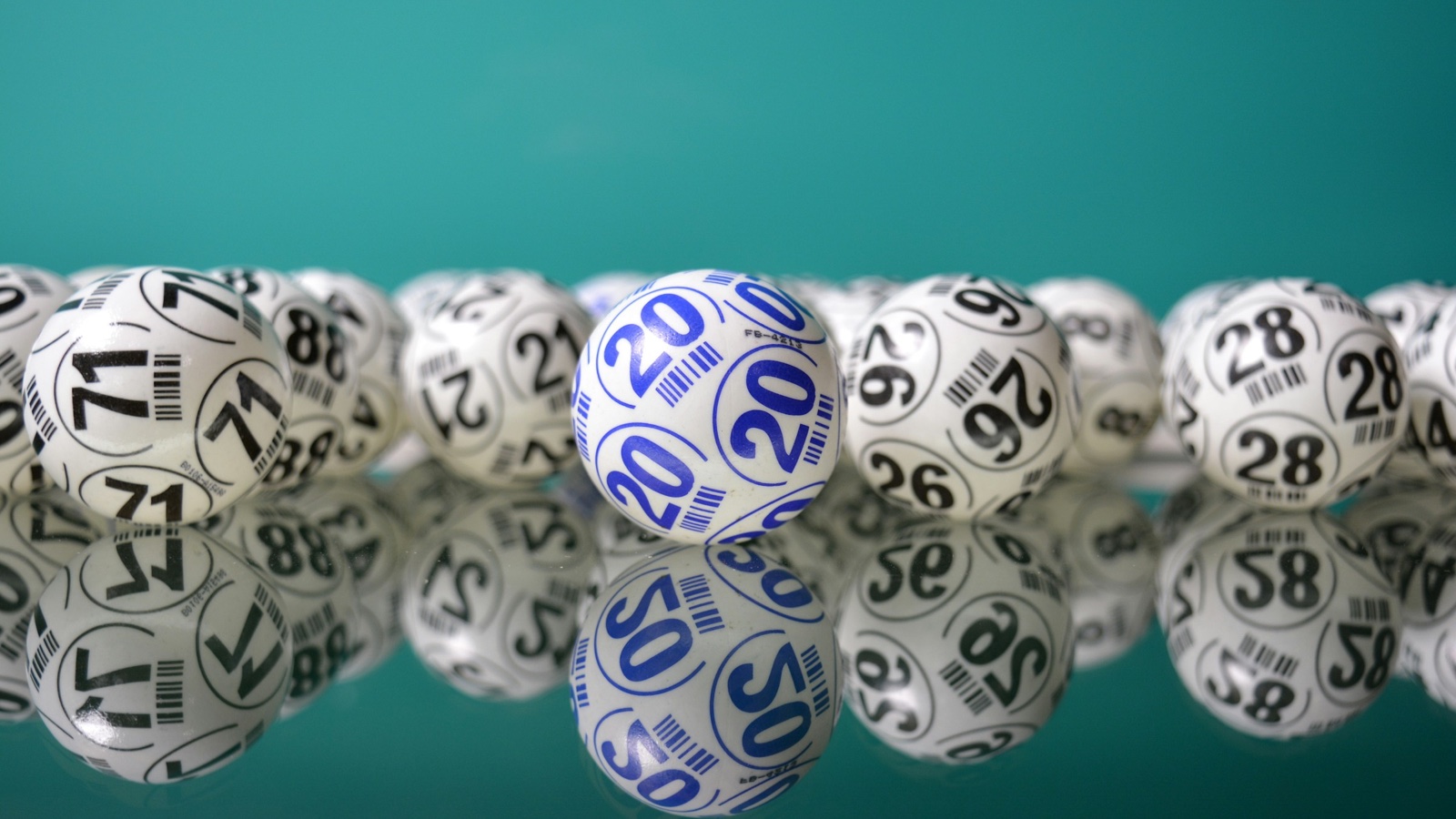 Numbered white lottery balls lined up on a glossy teal surface.