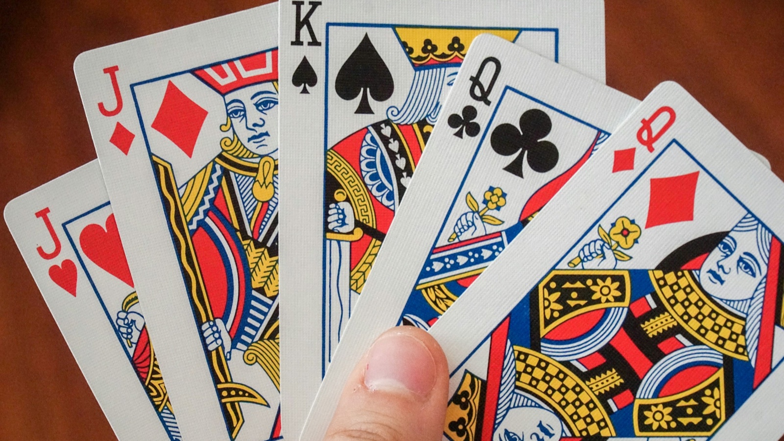 A hand holds a fanned set of playing cards showing jacks, a king and queens.