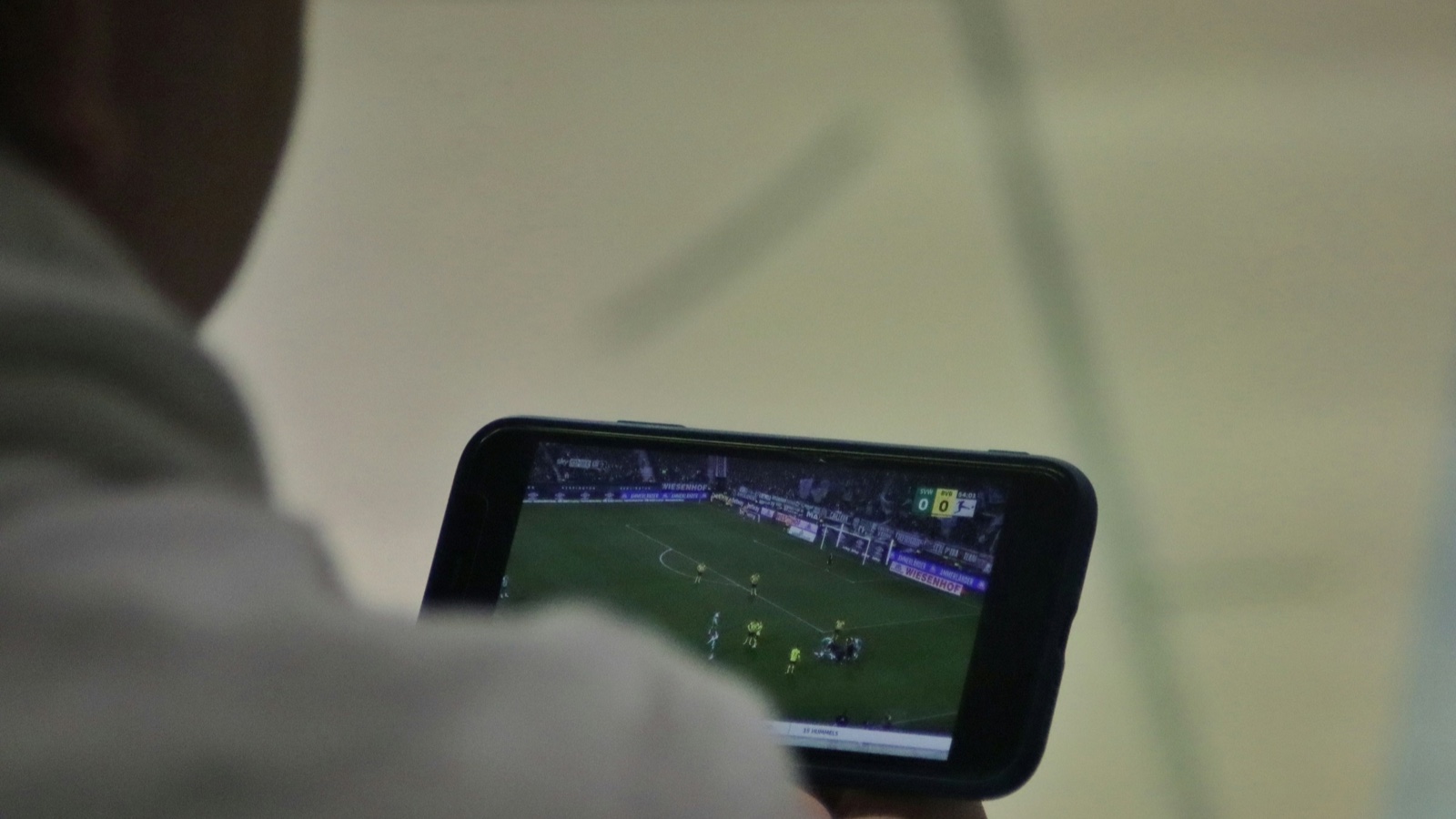 A man holds a phone on its side showing a live football match.