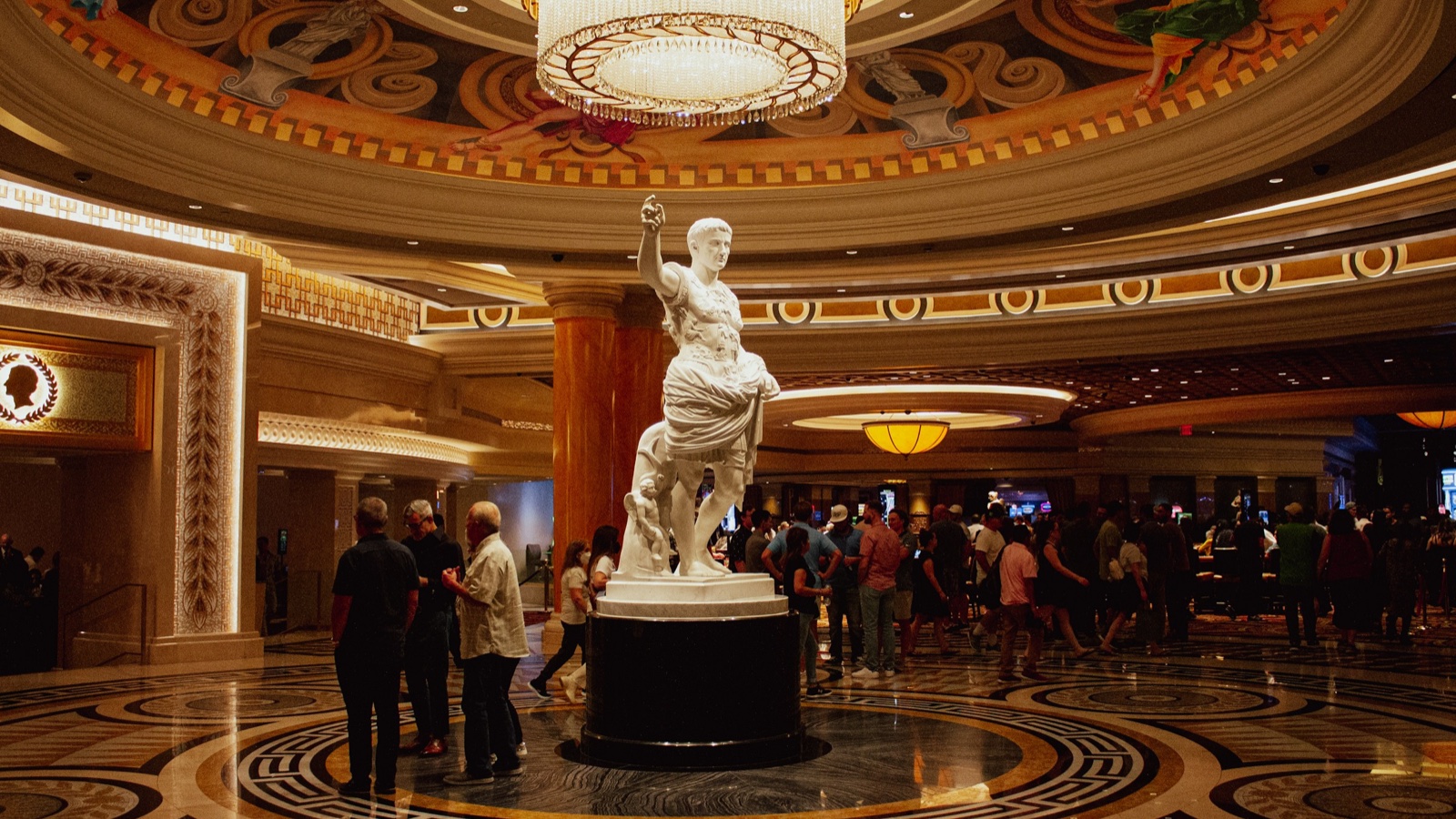 Visitors gather around a white marble statue under a chandelier in a Las Vegas casino lobby.