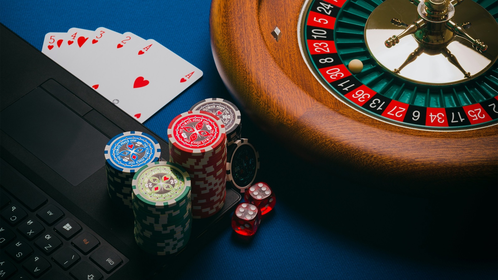 Poker chips, playing cards, dice and a roulette wheel sit beside a laptop keyboard.