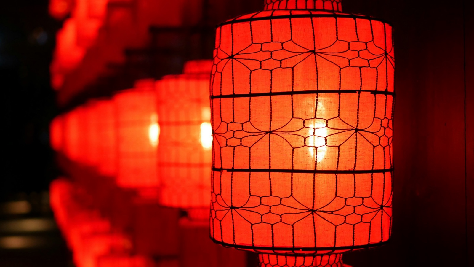 A glowing red paper lantern hangs in front of a row of blurred red lanterns in the dark.