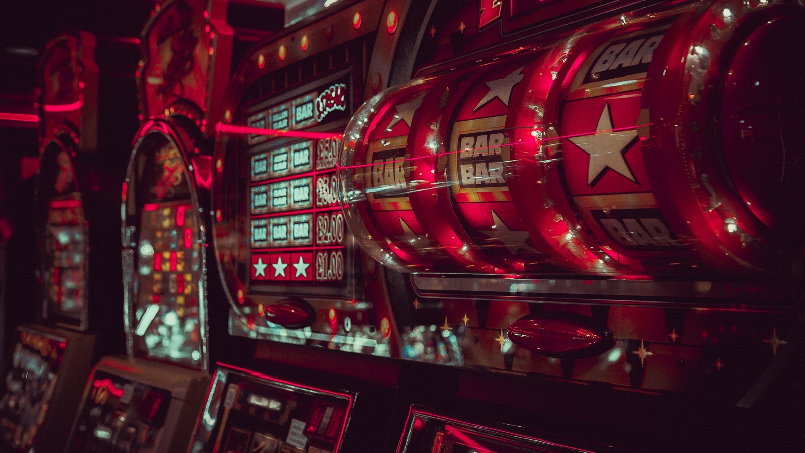 Close-up of glowing red slot machine reels showing stars and BAR symbols in a dark arcade.