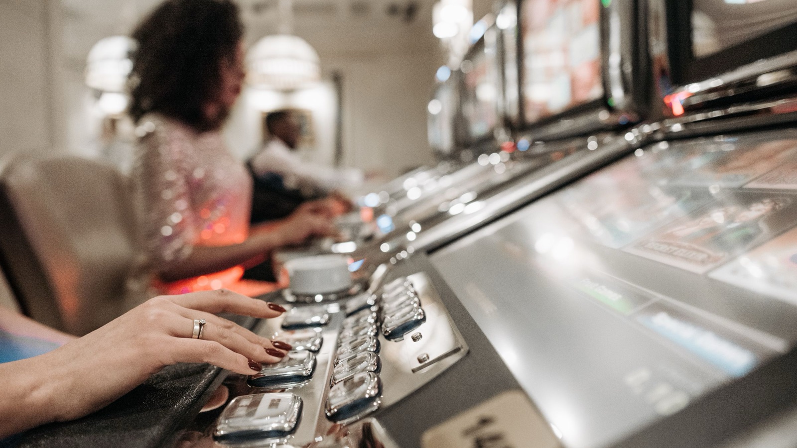 A woman's hand presses the row of buttons on a casino video poker machine while other players sit along the row.