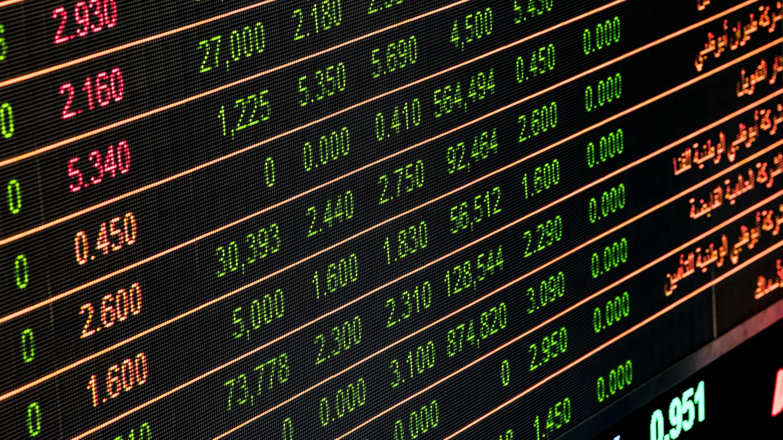 A close-up of a market price board with rows of green and red changing numbers on a dark screen.