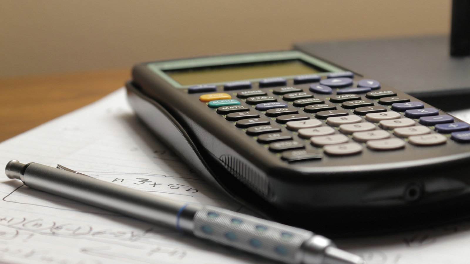 A calculator and a mechanical pencil resting on a notebook page covered in handwritten calculations.