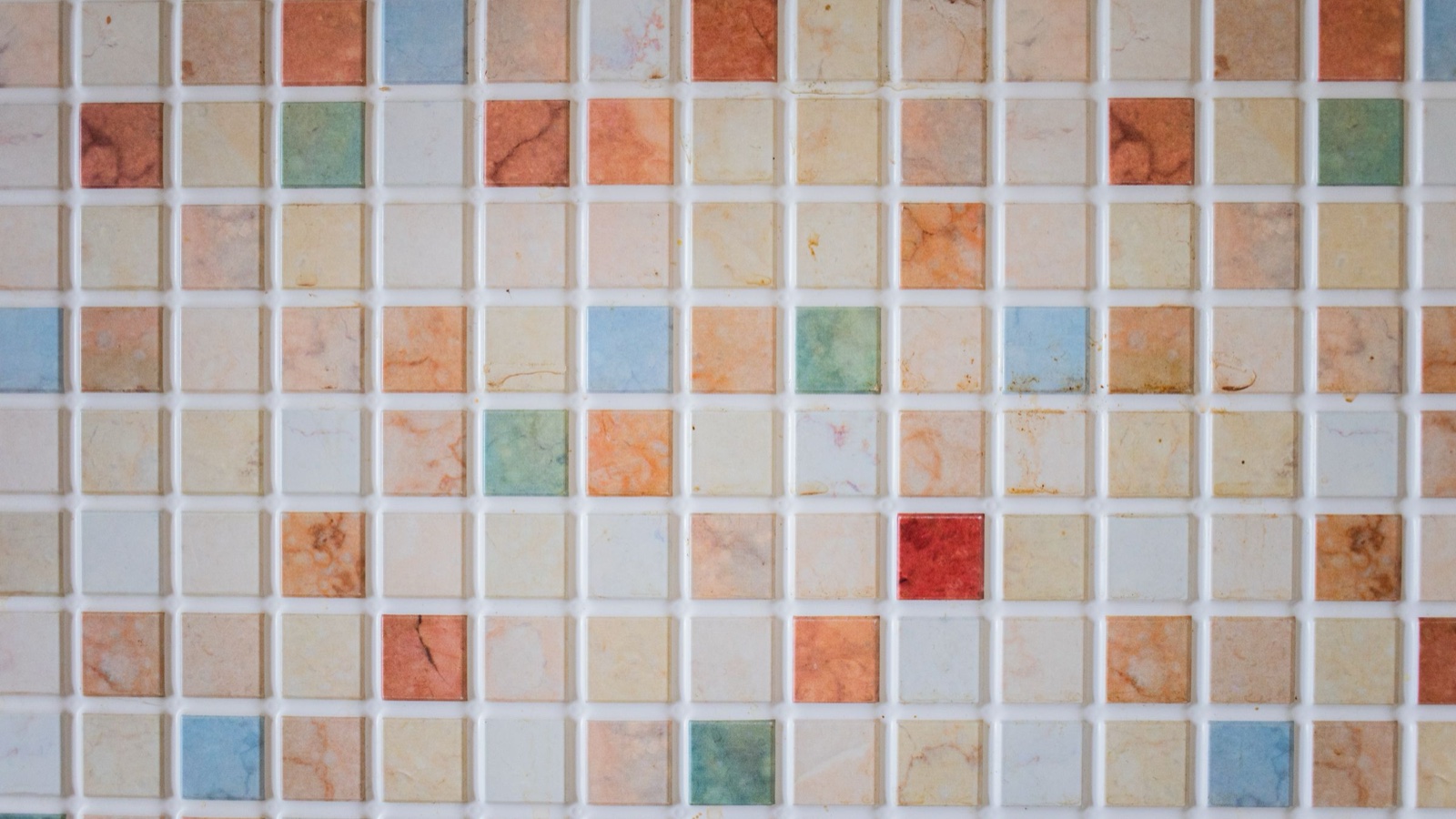 A wall of small square ceramic tiles in a grid, with one red tile standing out among the pale and orange ones.