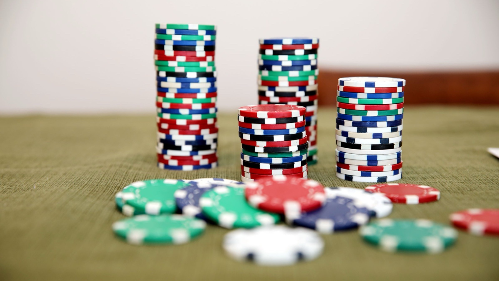 Towers of poker chips of different heights stand on a green cloth with loose chips in front.