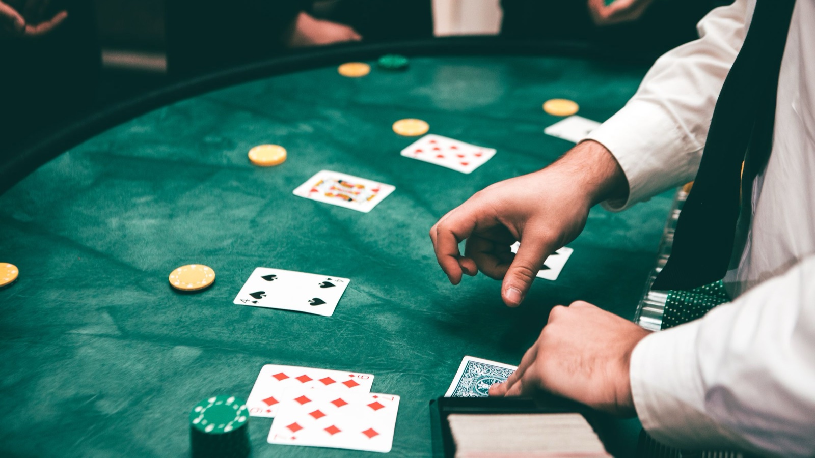 A dealer in a white shirt reaches over a green blackjack table with cards, chips and a card shoe.