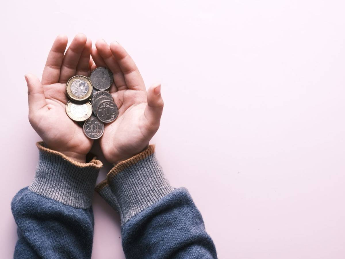 Two hands hold a small handful of coins against a pale pink background.