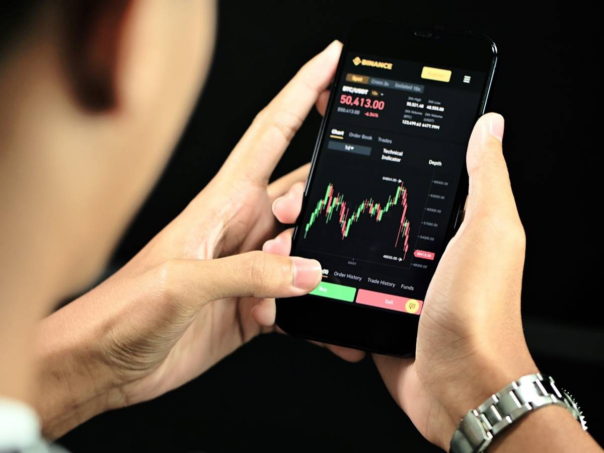 Two hands hold a smartphone showing a price chart on a trading app.