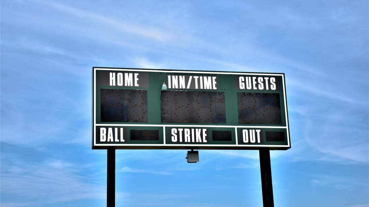 A green baseball scoreboard with blank digits for home, guests, inning, balls, strikes and outs against a blue sky.