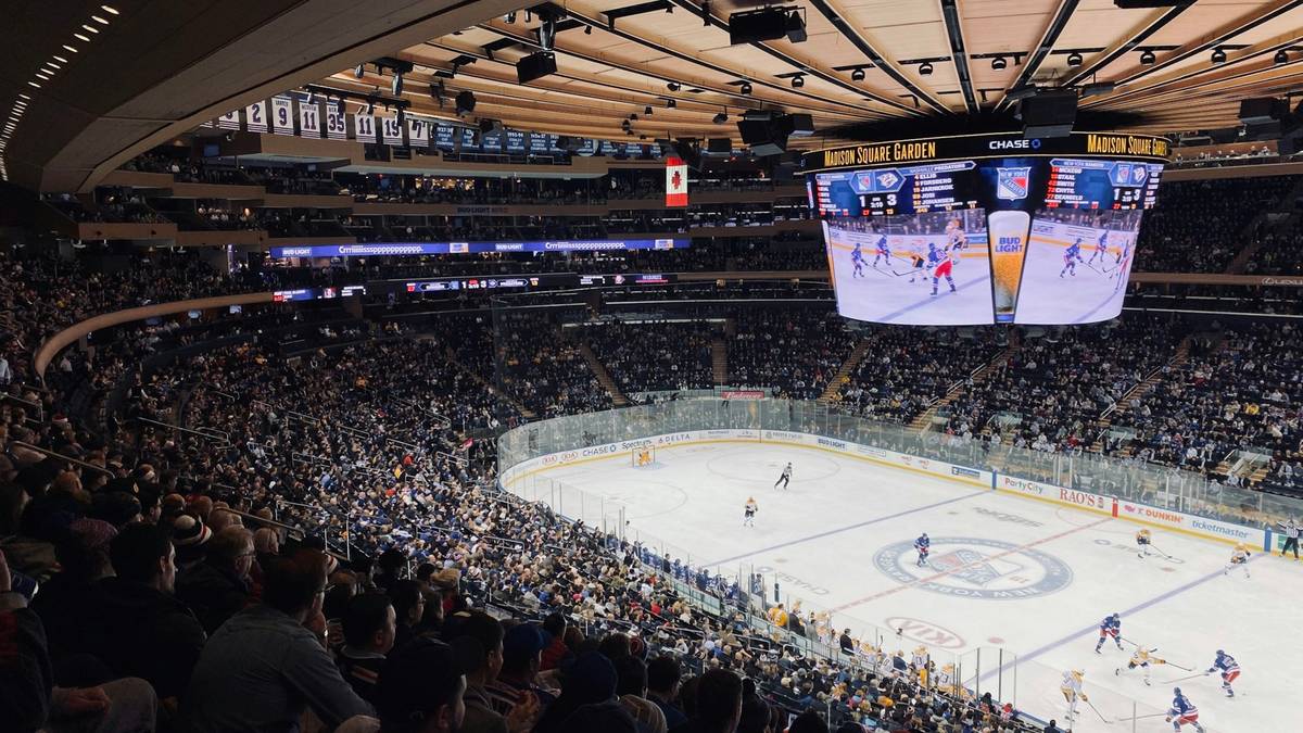 A packed ice hockey arena with a scoreboard hanging above the rink.