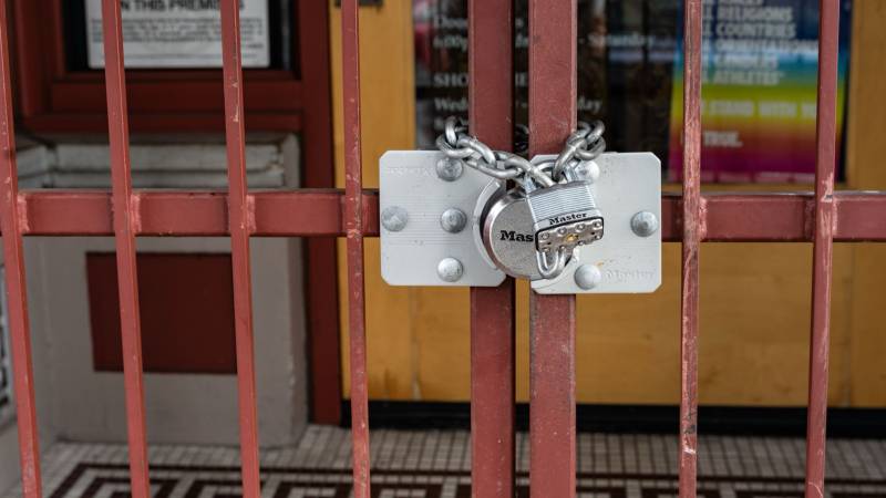 A chain and padlock fastened across the red bars of a closed gate in front of a locked doorway.