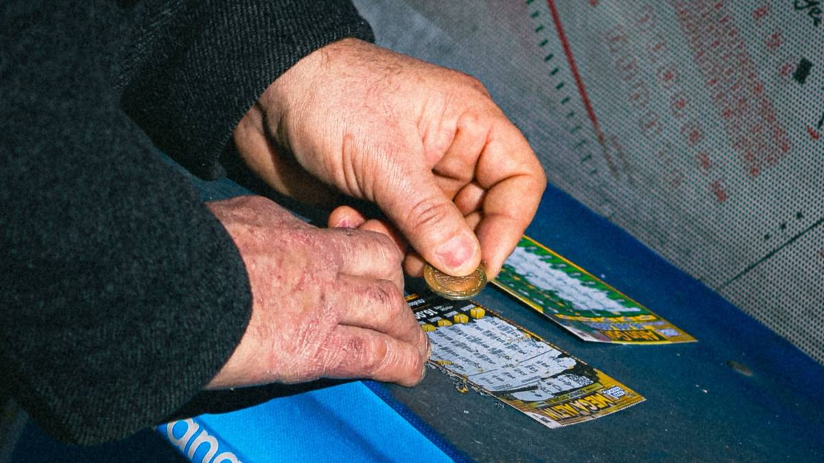 A pair of hands scratching a lottery scratch card with a coin.