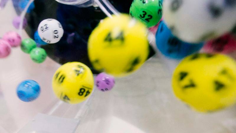 Colorful numbered lottery balls tumbling inside a clear plastic mixing machine.