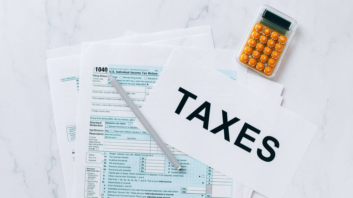 A US 1040 tax return form on a white desk with a pen, a small calculator and a sheet reading Taxes.