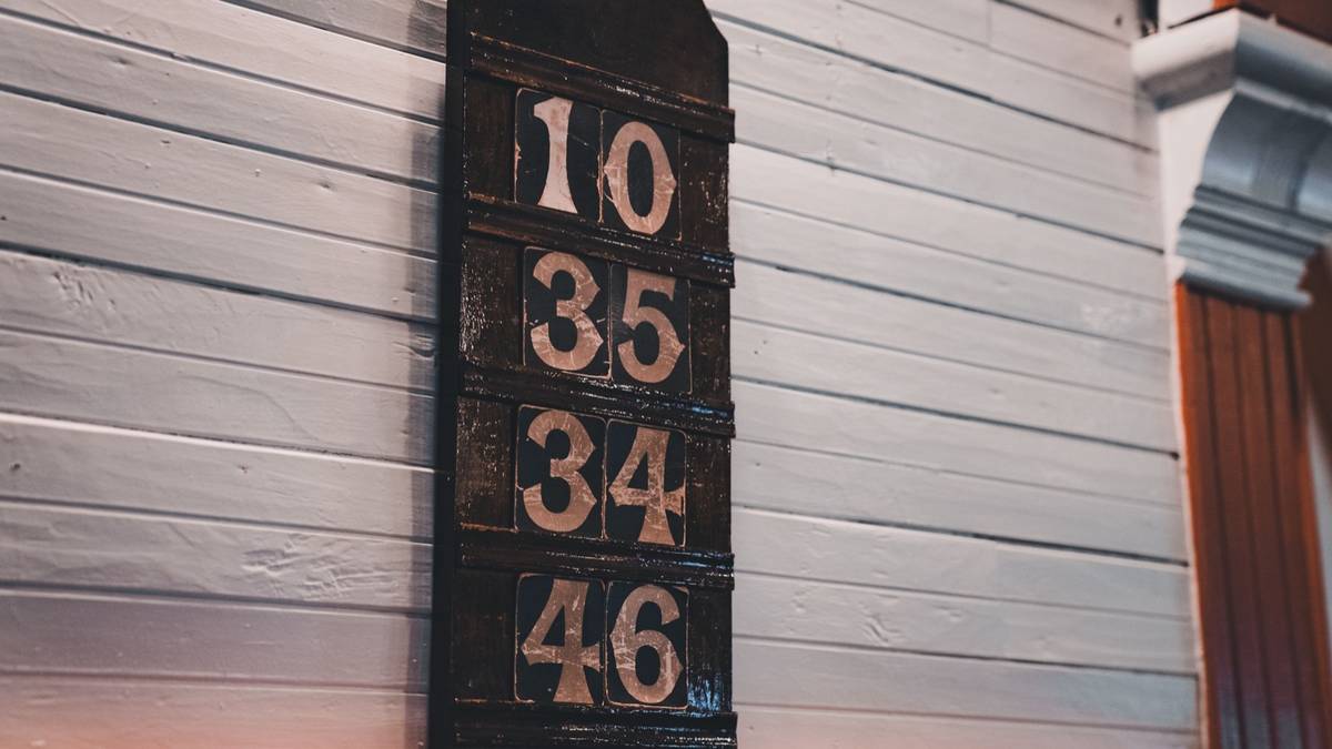 A black wall sign with four rows of large numbers on white wooden boards.