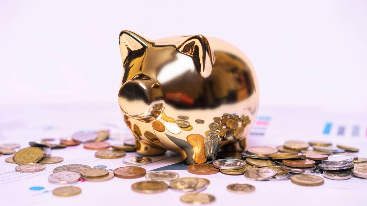A gold piggy bank surrounded by scattered coins and printed charts.