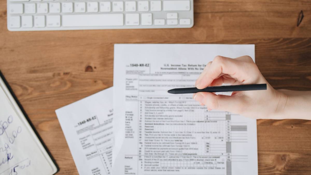 A hand holds a pen over a US tax return on a wooden desk.