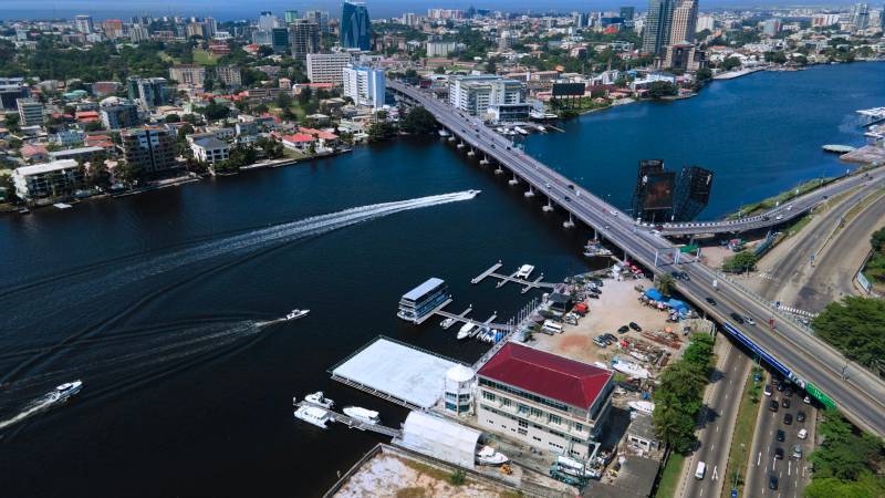 Aerial view of speedboats on a Lagos waterway beside a long road bridge and the city skyline.