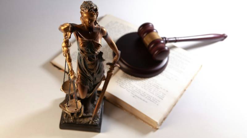A bronze statue of Lady Justice standing in front of a wooden gavel on an open law book.