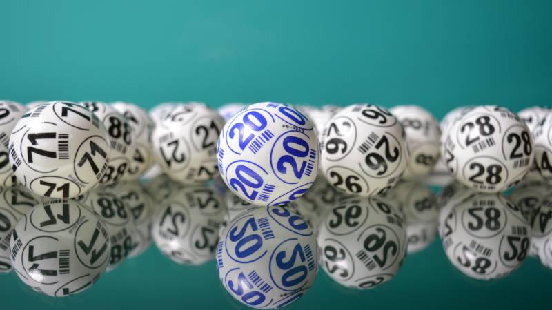 Numbered white lottery balls lined up on a glossy teal surface.