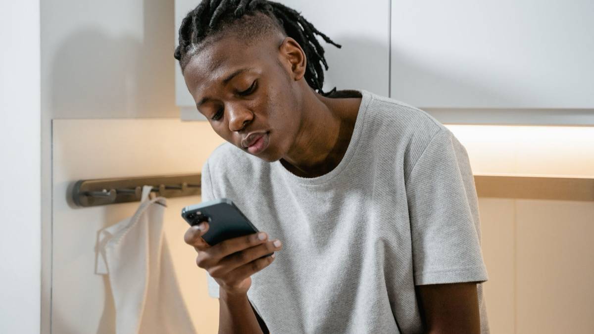 A young man in a grey t-shirt looks at his smartphone.