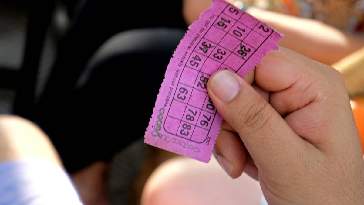 A hand holding a pink lottery ticket printed with a grid of numbers