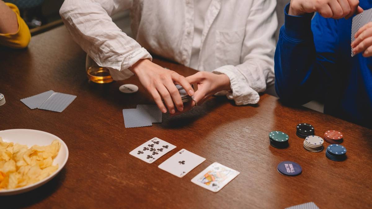 Players around a wooden table with a small stack of chips and cards laid face up.