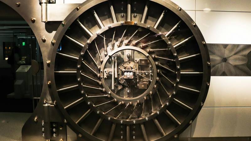 A large circular steel bank vault door with radiating locking bolts and a central lock mechanism.