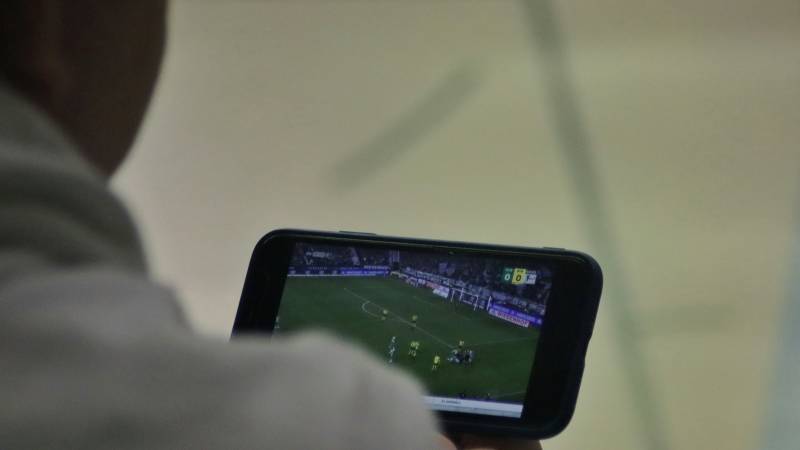 A man holds a phone on its side showing a live football match.