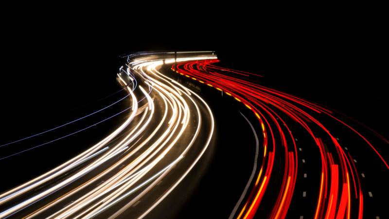 Long-exposure white and red light trails curve along a motorway at night.