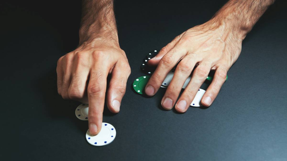 Two hands sliding casino chips across a dark table.