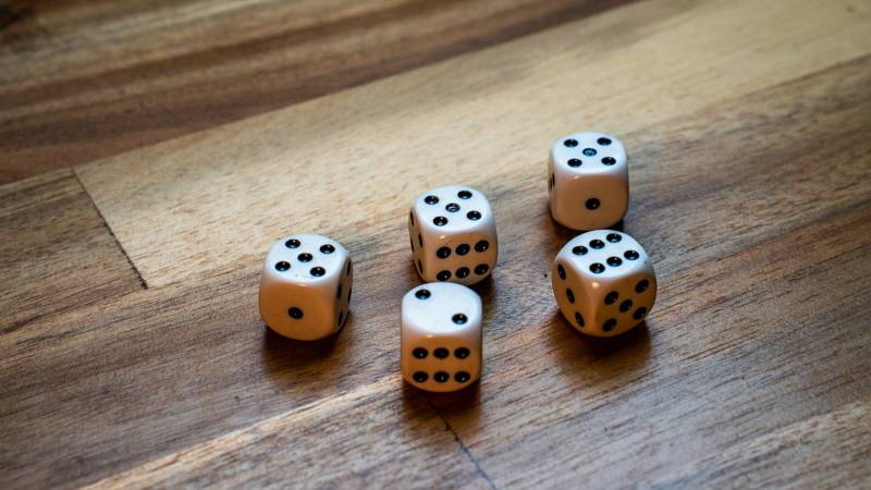 Five white dice scattered across a wooden table, each showing a different face.