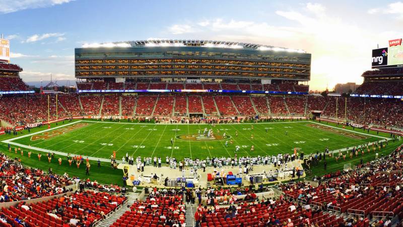 Panoramic view of a packed NFL stadium at dusk with a game under way on the field.
