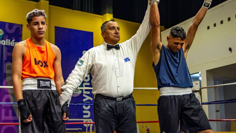 A boxing referee raises the winner's arm in the ring while the beaten boxer stands beside him.