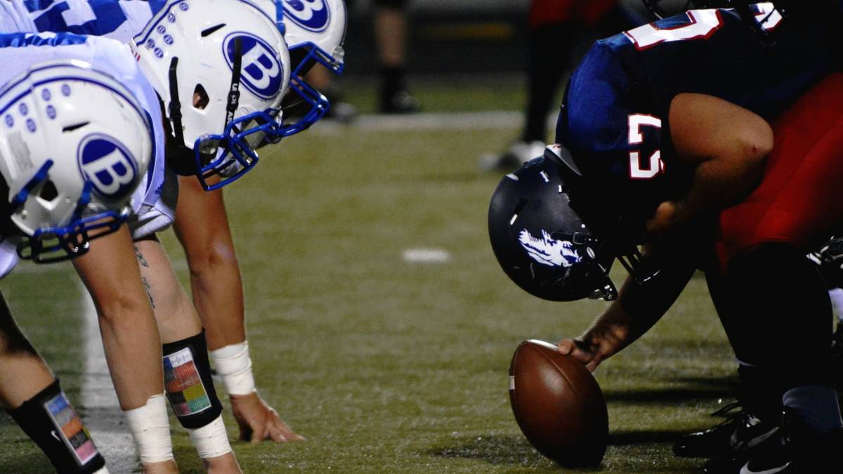 Two football linemen crouch face to face at the line of scrimmage with the ball between them.