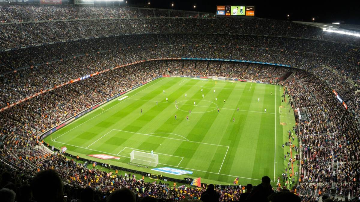 A packed floodlit soccer stadium at night with the players spread across a bright green pitch.