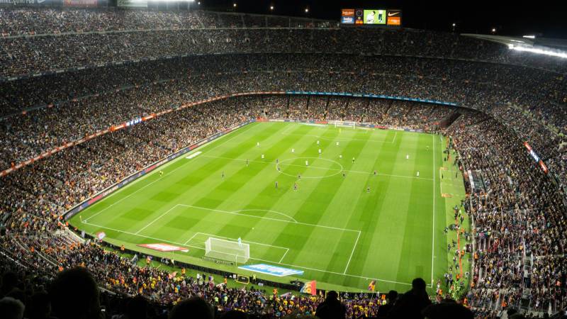 A packed floodlit soccer stadium at night with the players spread across a bright green pitch.