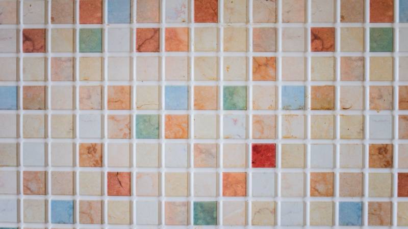 A wall of small square ceramic tiles in a grid, with one red tile standing out among the pale and orange ones.