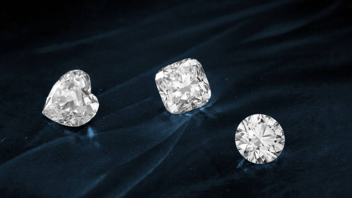 Three cut diamonds lying on dark blue fabric.