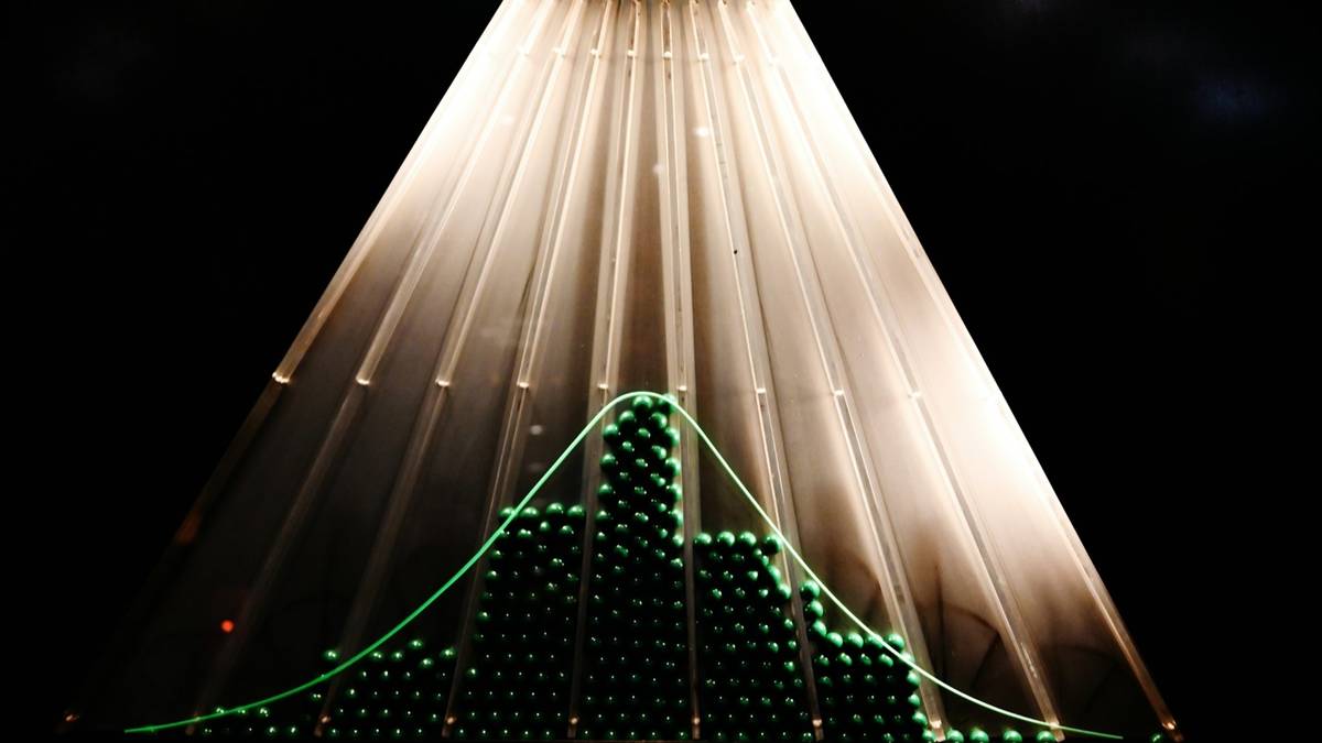 A Galton board with lit beads dropping through rows of pins and piling into a bell curve at the bottom