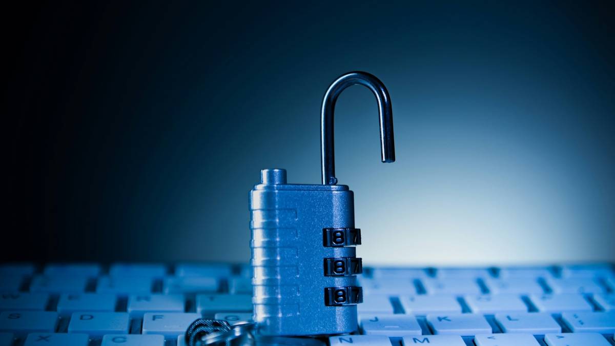 An open combination padlock standing on a computer keyboard in blue light.